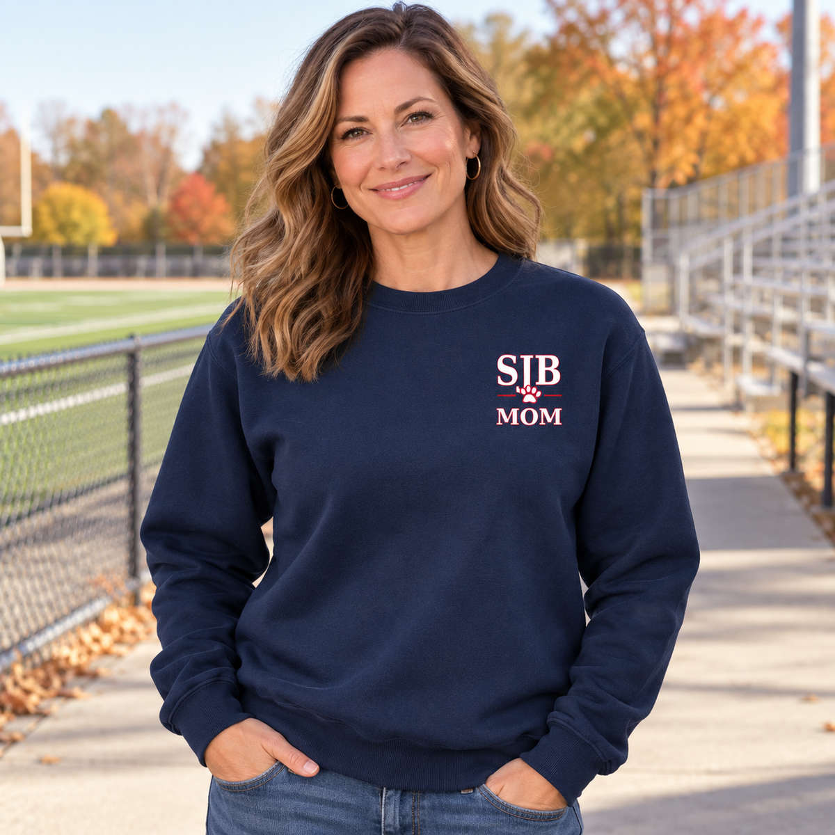 Adult woman wearing navy SJB Mom crewneck at a football field